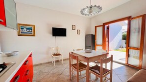 Una cocina compacta con comedor, un televisor montado en la pared y un ventanal corredero que da a un espacio exterior.