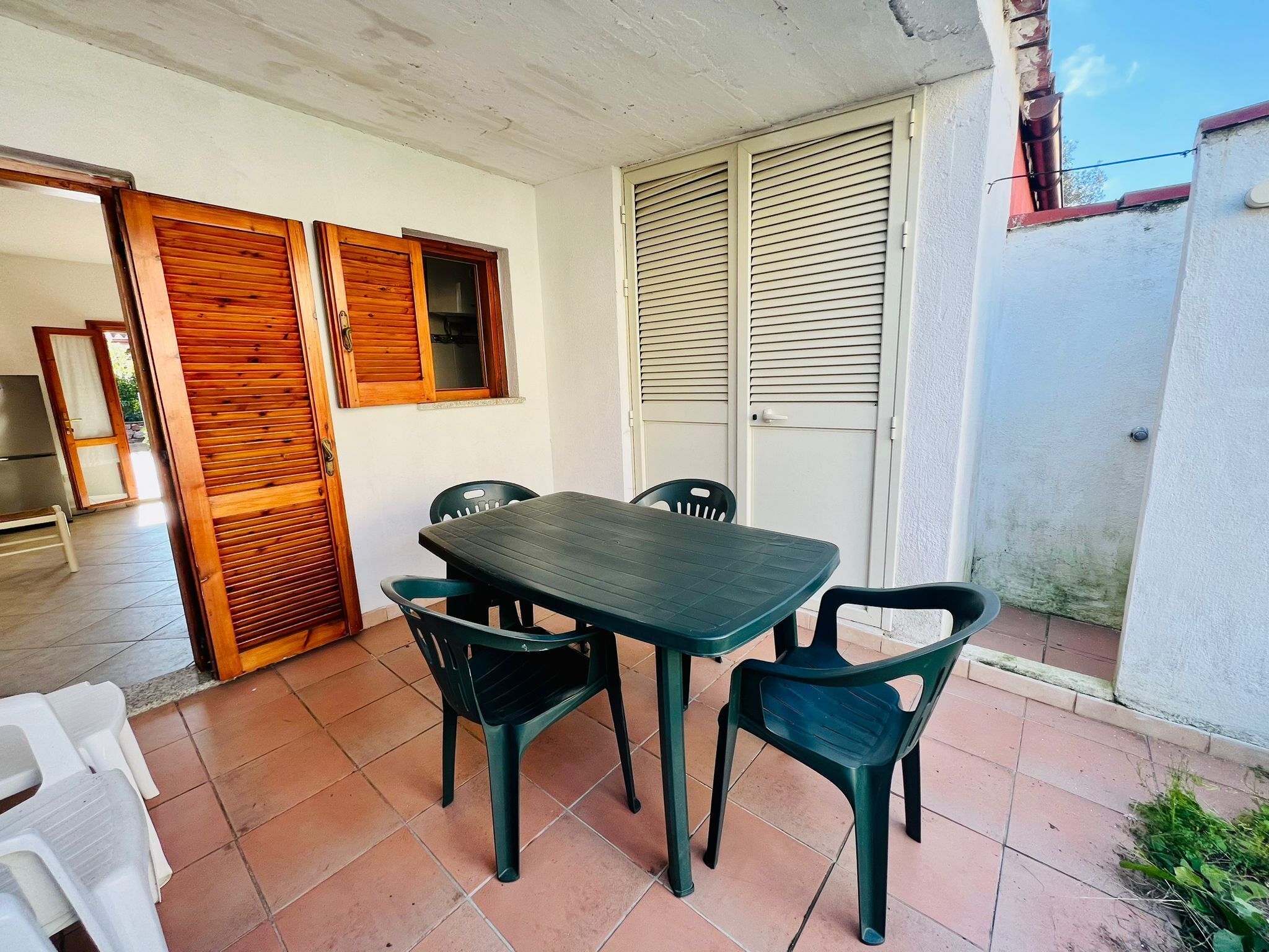 Um pátio com mesa e cadeiras, uma porta deslizante e uma janela com venezianas de madeira.