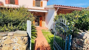 Una casa de dos pisos con un sendero de piedra que conduce a la entrada, rodeada de follaje y un portón de metal.