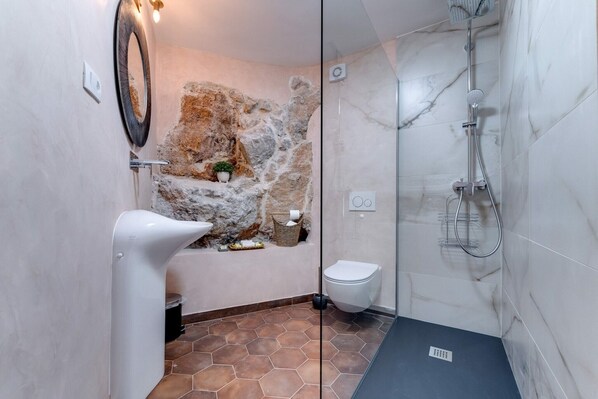 A bathroom with a stone wall, a modern sink, a toilet, and a glass-enclosed shower area. - Villa with panoramic view of the sea (Vrbnik)