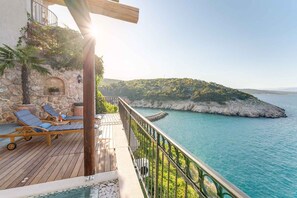A wooden deck with lounge chairs, a stone wall, and a view of the sea and a rocky island. - Villa with panoramic view of the sea (Vrbnik)