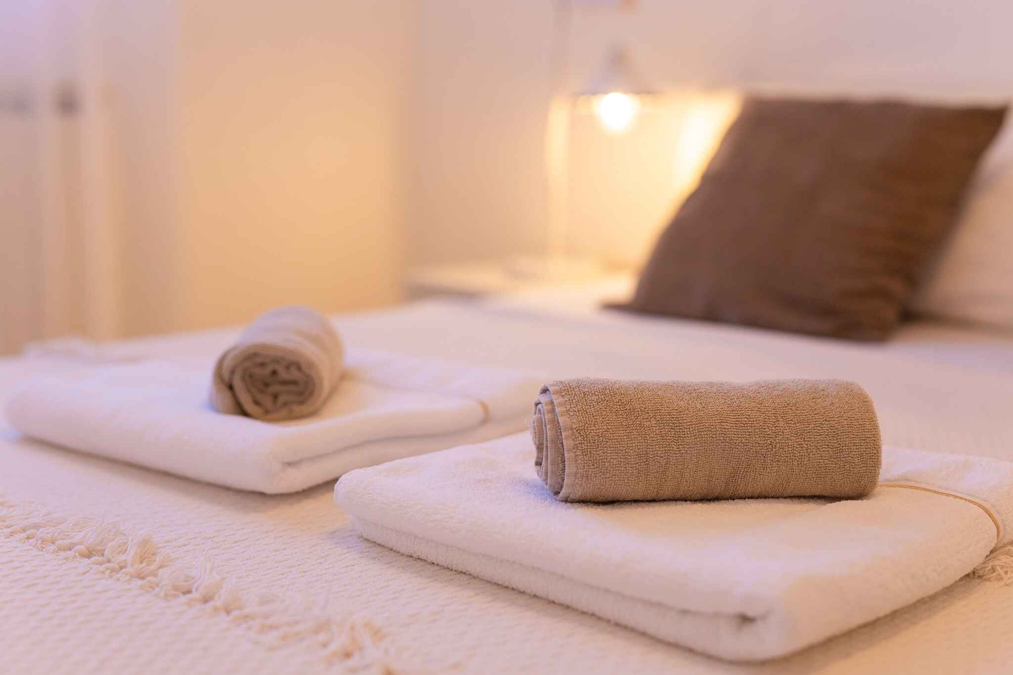 A neatly made bed with two rolled towels and a brown pillow.