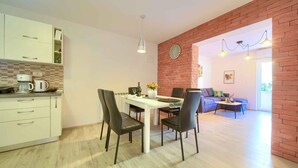 A modern kitchen with white cabinets, a dining table with four chairs, and a brick accent wall. - Holiday apartment with terrace near the beach (Vrbnik)