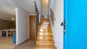 A wooden staircase leading to a room with a blue door, a stone wall, and a dining area with chairs and a table. - Holiday home in an old town (Vrbnik)