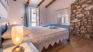 A bedroom with a bed, a bedside lamp, a stone wall, and a window with curtains. - Holiday home in an old town (Vrbnik)