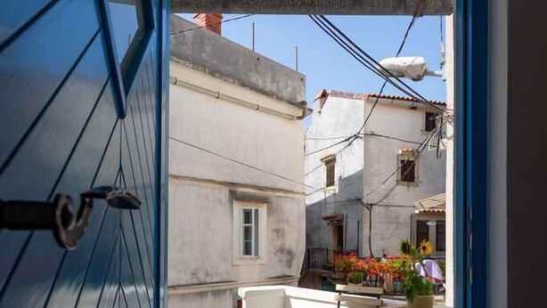 A narrow alleyway with a blue door leading to a courtyard. A welcome mat is visible at the entrance, and there are potted plants and a small table with chairs outside. - Holiday home in an old town (Vrbnik)