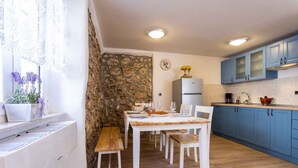 A dining area with a stone wall, wooden table, and blue cabinets. - Holiday home in an old town (Vrbnik)
