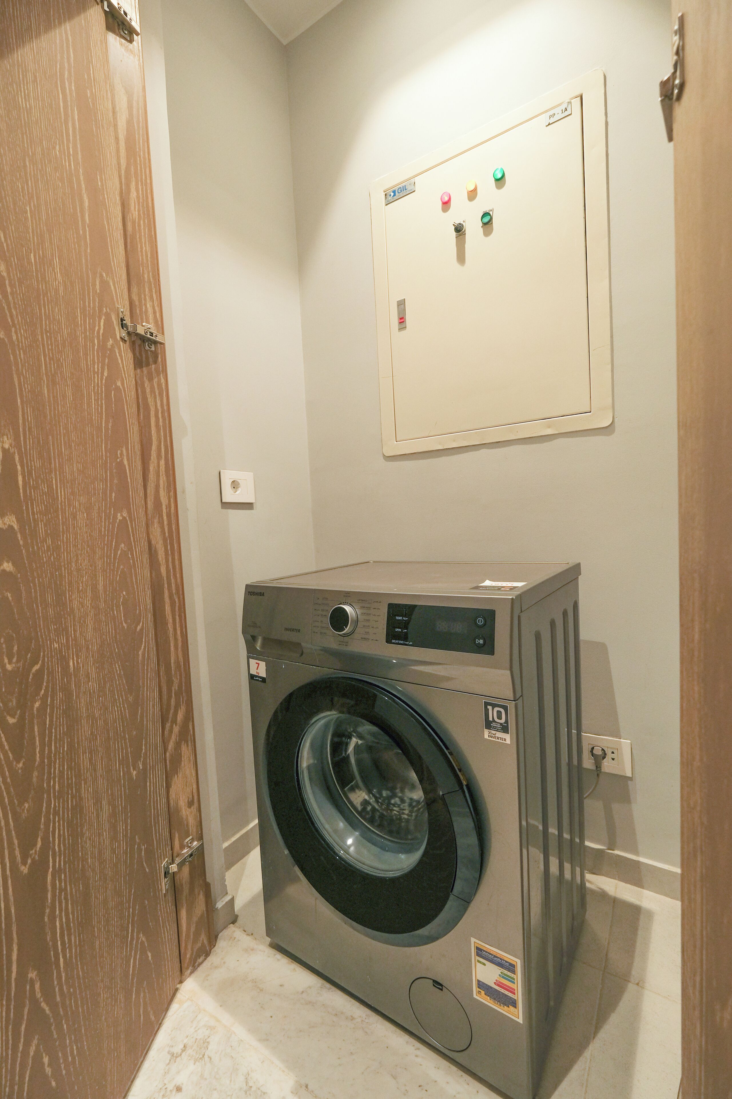 A compact, modern laundry room with a front-loading washing machine, a control panel with various buttons, and a wooden door.