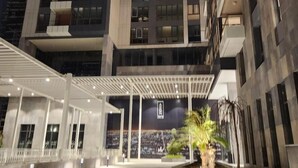Un edificio moderno de varios pisos con un área de entrada cubierta y un jardín ajardinado.