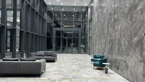 Un hall d’entrée moderne avec un sol en marbre, des canapés gris et un fauteuil turquoise.