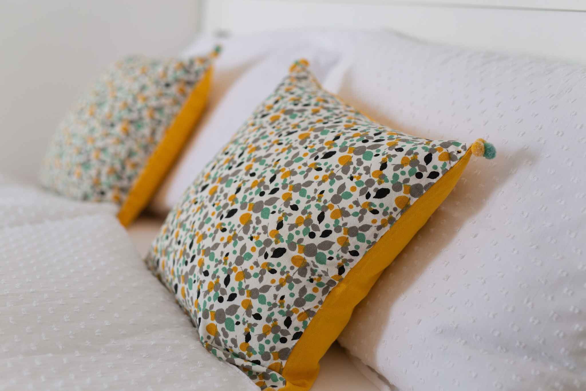Un letto con biancheria bianca e due cuscini decorati con un motivo variegato e bordi gialli.