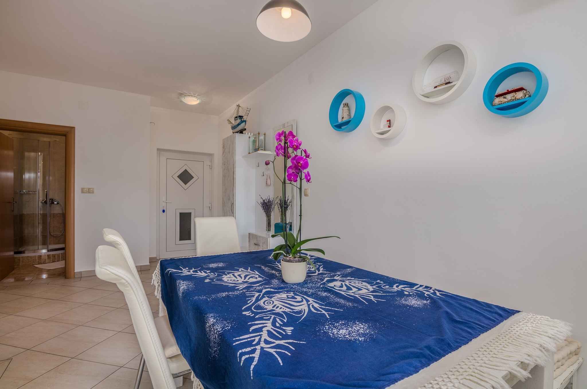A dining area with a table covered in a blue tablecloth, white chairs, and a potted plant.