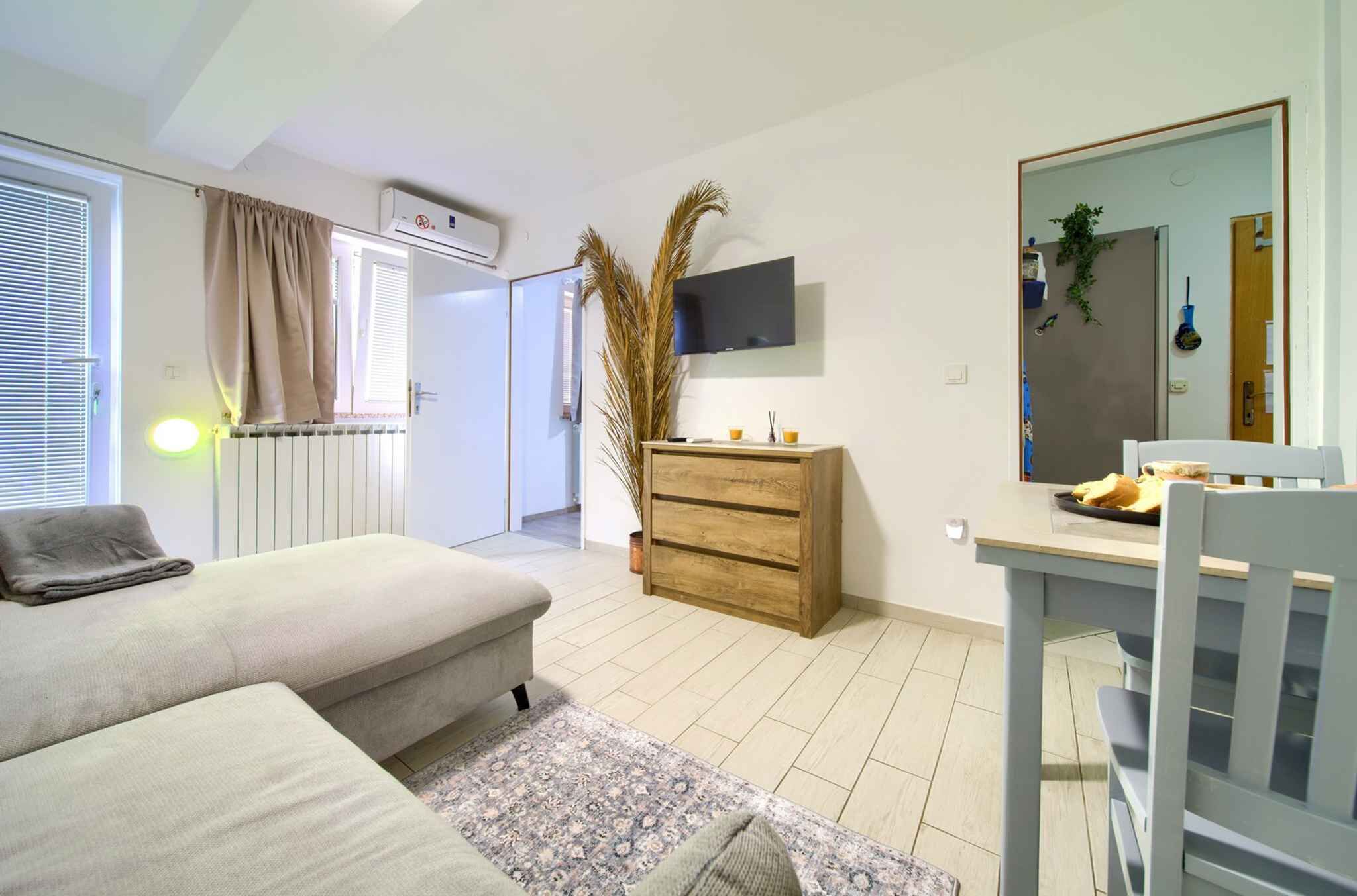 A modern bedroom with a sofa, a wooden dresser, a TV mounted on the wall, and a dining table with chairs.