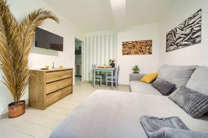 Uma sala de estar moderna com sofá, cômoda de madeira, mesa de jantar com cadeiras e televisão na parede.