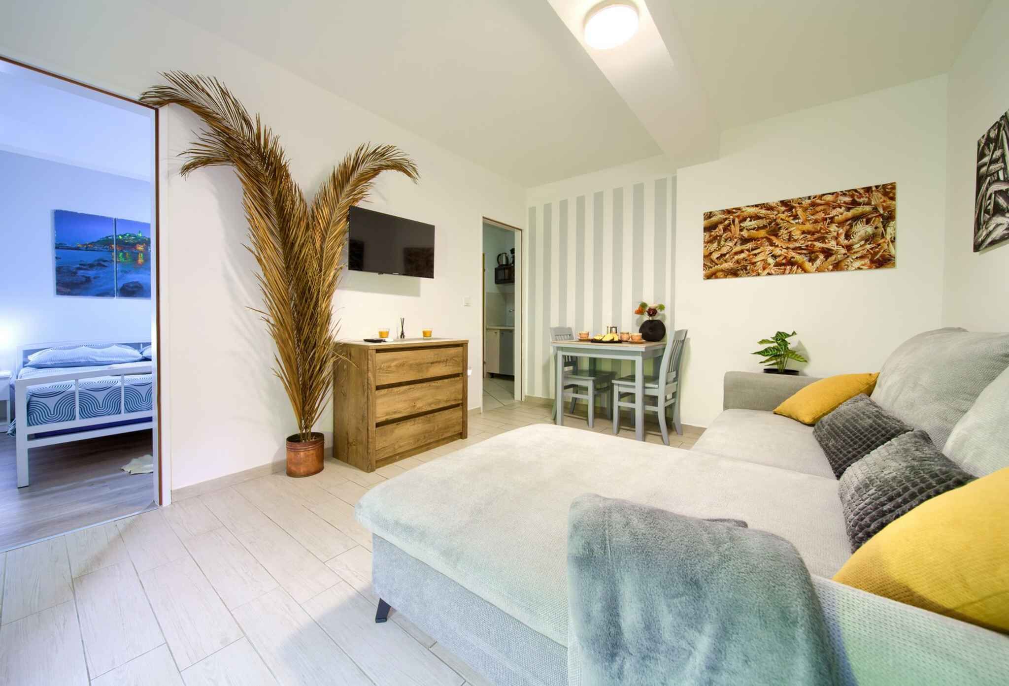 Una sala de estar moderna con un sofá, una mesa de comedor y un televisor. Hay una cama en la habitación contigua.