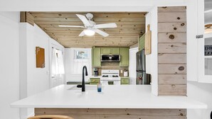 Eine moderne Küche mit weißen Arbeitsplatten, grünen Schränken und einer Holzbalkendecke.