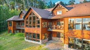 A multi-story log cabin with large windows and balconies, surrounded by a forested landscape. - Bay Ridge North Lakeshore Lodge Retreat (Park Rapids)