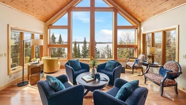A spacious room with a high ceiling, large windows offering a view of trees and mountains, and a cozy seating area with sofas and a coffee table. - Bay Ridge North Lakeshore Lodge Retreat (Park Rapids)