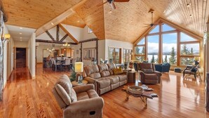 A spacious living room with a high ceiling, wooden beams, and large windows offering a view of the outdoors. - Bay Ridge North Lakeshore Lodge Retreat (Park Rapids)