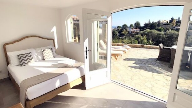 Un dormitorio con cama, puerta que da a un balcón con sillones de descanso y vistas del paisaje.