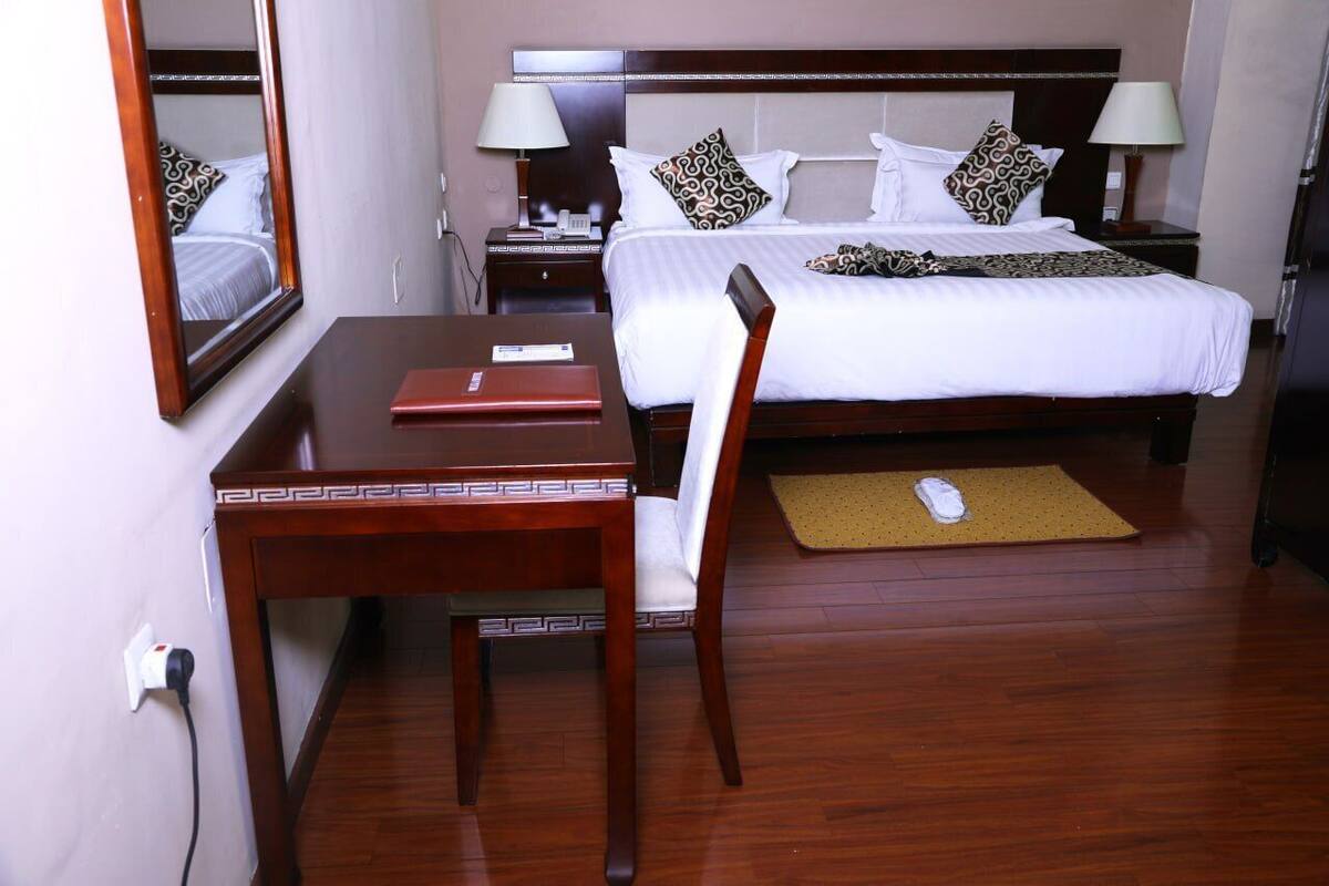 Une chambre d’hôtel comprenant un lit, des tables de chevet, un bureau, une chaise, un miroir et une lampe de chevet.