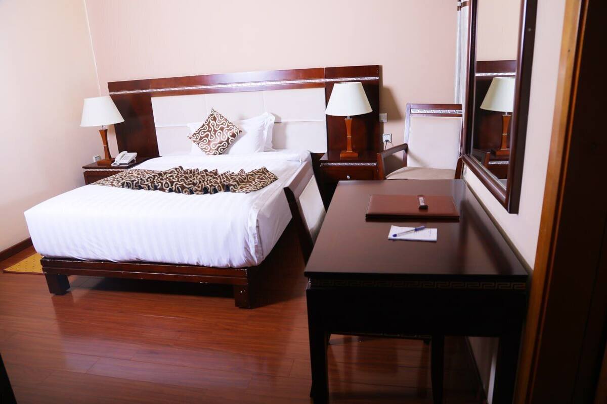 Une chambre d’hôtel avec un lit en bois, deux tables de chevet avec des lampes, un bureau et un grand miroir.