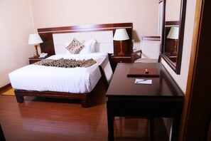 A hotel room with a wooden bed, two bedside tables with lamps, a desk, and a large mirror. - Melka International Hotel (Addis Ababa)