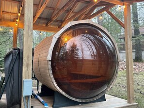 Eine große Hollfass-Konstruktion mit Glasglocke, umgeben von einer Holzterrasse und einem überdachten Bereich mit Lichterketten.
