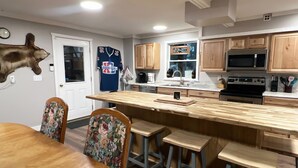 A modern kitchen with wooden cabinets, a large island with stools, a mounted deer head, and a Super Bowl jersey on the wall. - 4-bedroom two level guest house next to Shupac Lake in Grayling (Grayling)