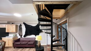 A living room with a wooden staircase, a leather sofa, a black lamp, and a mounted animal hide. - 4-bedroom two level guest house next to Shupac Lake in Grayling (Grayling)
