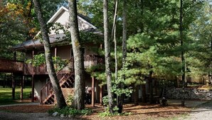 A cabin with a wooden deck, surrounded by trees. - 4-bedroom two level guest house next to Shupac Lake in Grayling (Grayling)