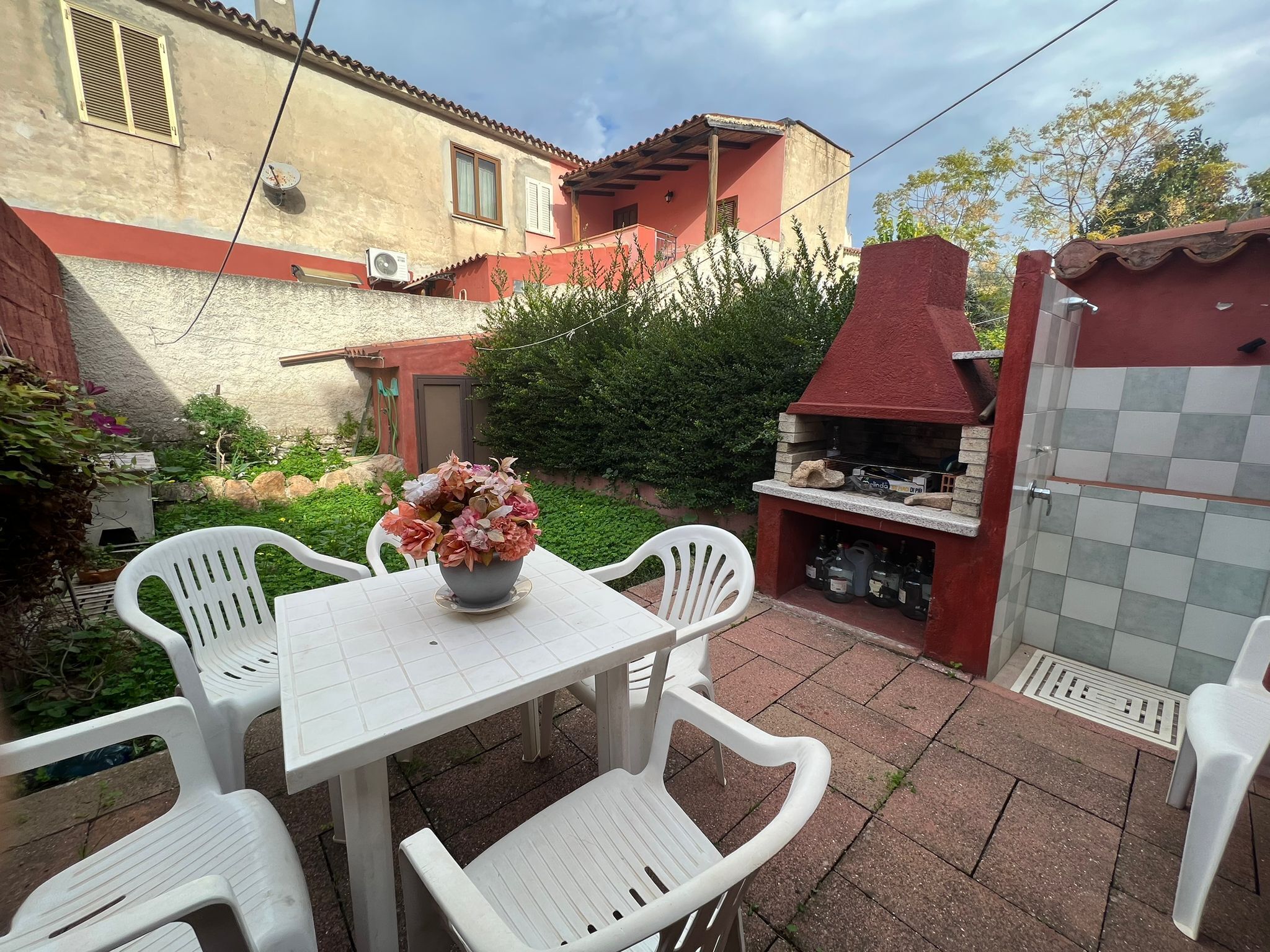A patio with a table and chairs, a barbecue grill, and a flower vase.