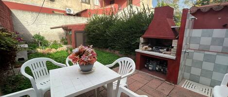 A patio with a table and chairs, a barbecue grill, and a flower vase.