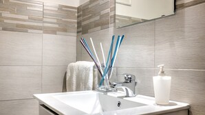 Ein Badezimmer mit einem weißen Waschbecken, einem Chrom-Wasserhahn und einer Glas-Seifenspender. In einem Halter befinden sich blaue und weiße Zahnbürsten.