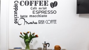 Eine Wand mit einem Schild zum Thema Kaffee, das verschiedene Kaffeesorten auflistet, sowie ein Tisch mit Kaffeekanne, Tassen und einem Strauß Tulpen.