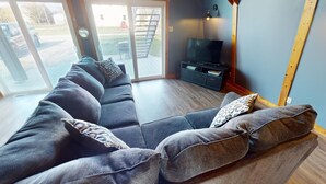 A modern living room with a sectional sofa, a flat-screen TV, and a sliding glass door leading to an outdoor area.