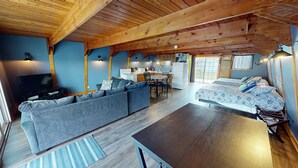 A cozy cabin-style room with a sofa, a bed, a dining table, and a kitchen area.