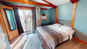 A bedroom with a bed, a window, a door, and a sign on the wall.