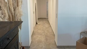 Un couloir avec un sol carrelé, une commode en bois et une plante en pot.
