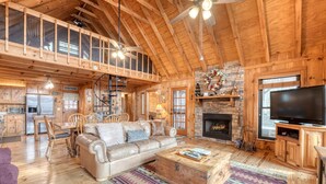 Ein geräumiges Blockhaus-Interieur mit hohen Decken, Kamin, Fernseher und Essbereich.
