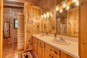 Une salle de bain en bois avec deux lavabos, un grand miroir et des luminaires fixés au mur.