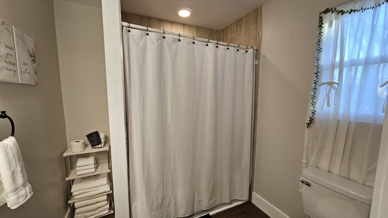 Un baño con cortina de ducha, inodoro y estante con toallas y artículos de aseo.