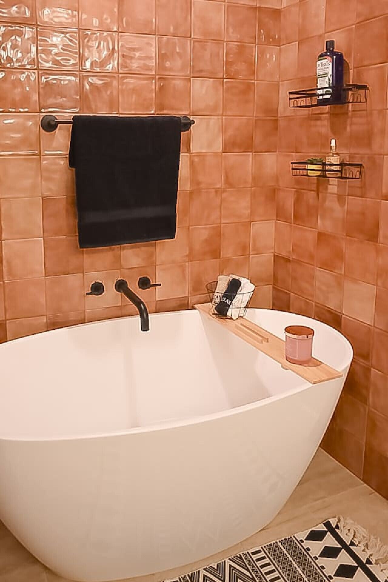 A modern bathroom with a freestanding bathtub, a black towel hanging on a rack, and a small shelf with toiletries.