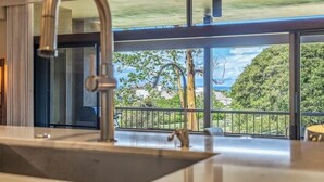 Eine moderne Küche mit einem großen Fenster, einer Edelstahl-Spüle und Blick auf eine grüne Landschaft.