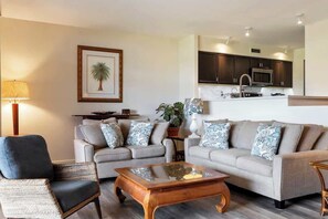 Un salon avec deux canapés, une table basse, un fauteuil, une lampe et un tableau encadré au mur.