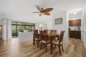 Zona pranzo con tavolo e sedie in legno, ventilatore a soffitto e vista sull'esterno.