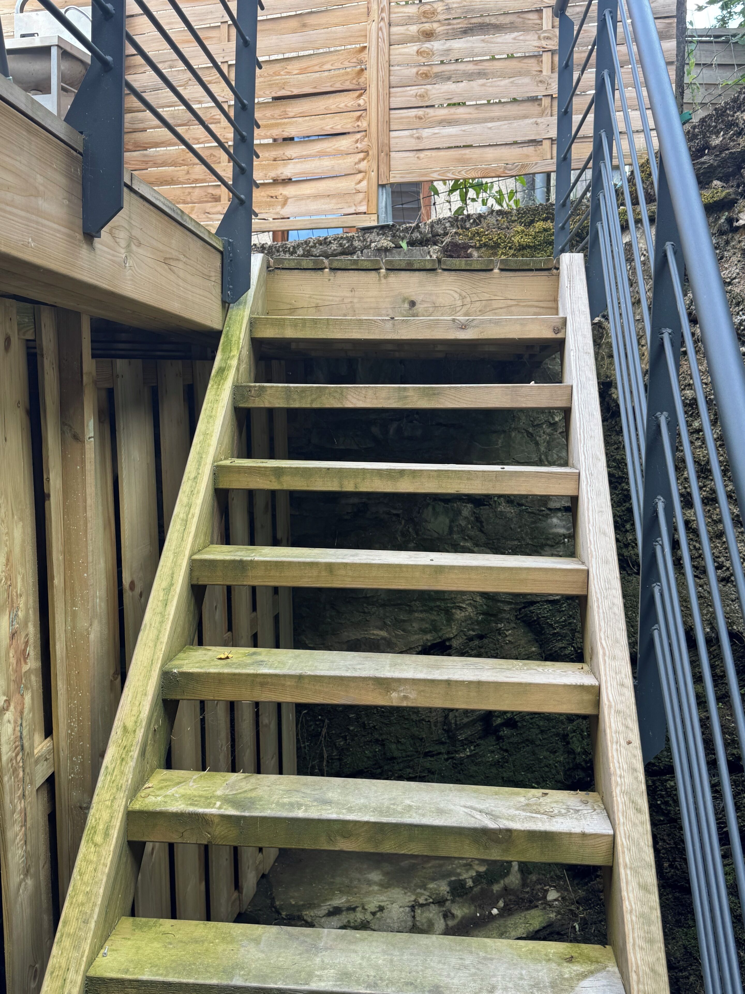 Una escalera de madera con barandillas metálicas que conduce a una cubierta de madera.