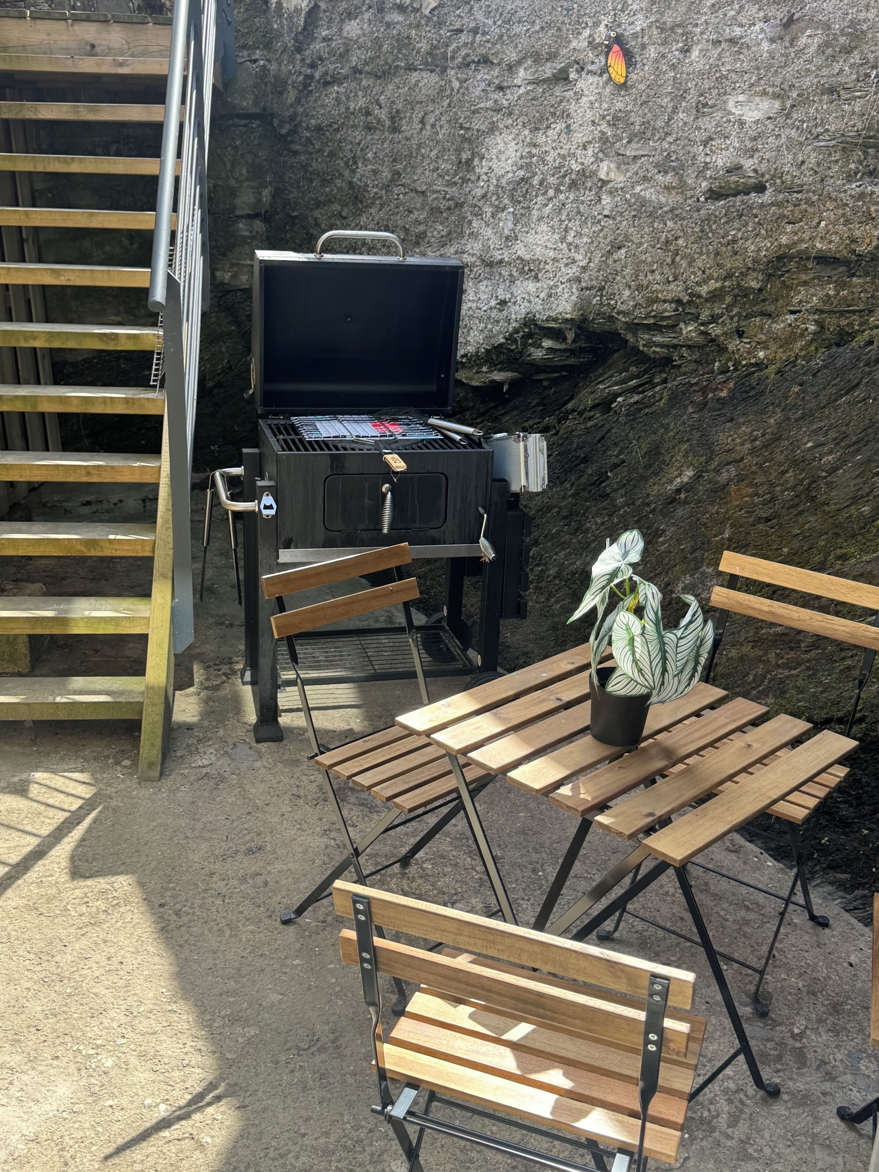 Un espace extérieur aménagé avec un barbecue, des bancs en bois et un pot de fleurs.