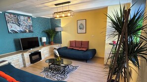 A living room with a sofa, a coffee table, a fireplace, a TV, and a plant.