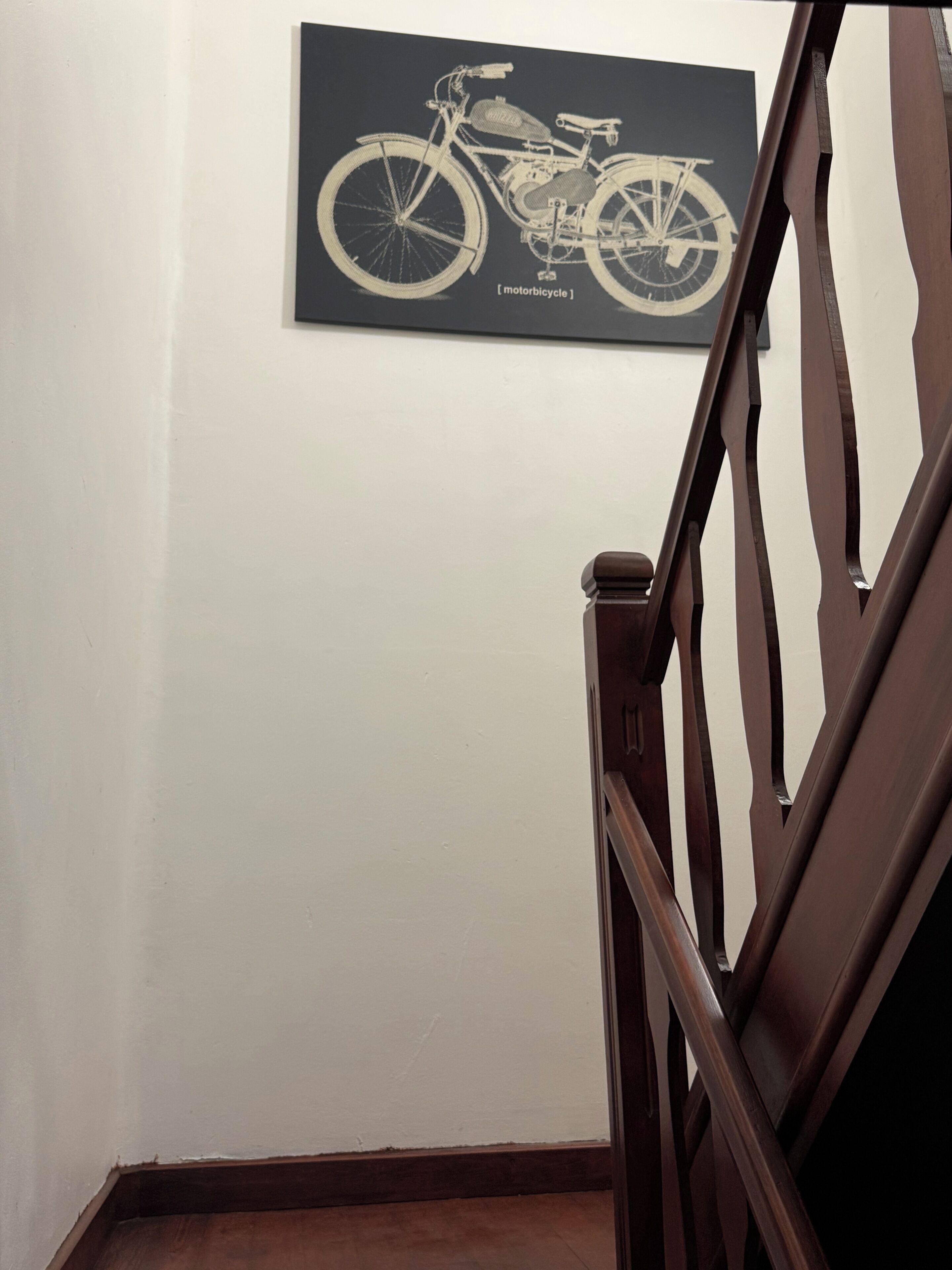 Een trap met een houten leuning en een aan de muur hangend schilderij van een motor.